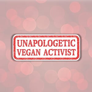 May include: Red rubber stamp with the text "Unapologetic Vegan Activist" on a pink background with a bokeh effect.