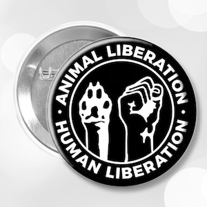 May include: Black and white button with the text "Animal Liberation. Human Liberation." in a circle. Inside the circle is a raised fist and a paw print.
