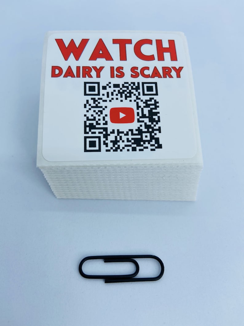Pode incluir: Uma pilha de adesivos quadrados brancos com texto vermelho que diz "WATCH DAIRY IS SCARY" e um c&oacute;digo QR preto e branco com um bot&atilde;o de reprodu&ccedil;&atilde;o vermelho no centro. Um clipe de papel preto est&aacute; no centro inferior da imagem.