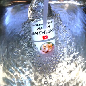 May include: A clear glass bottle with a white label that says "You've been lied to. Watch Earthling" with a YouTube logo. The bottle is submerged in water with bubbles forming around it.