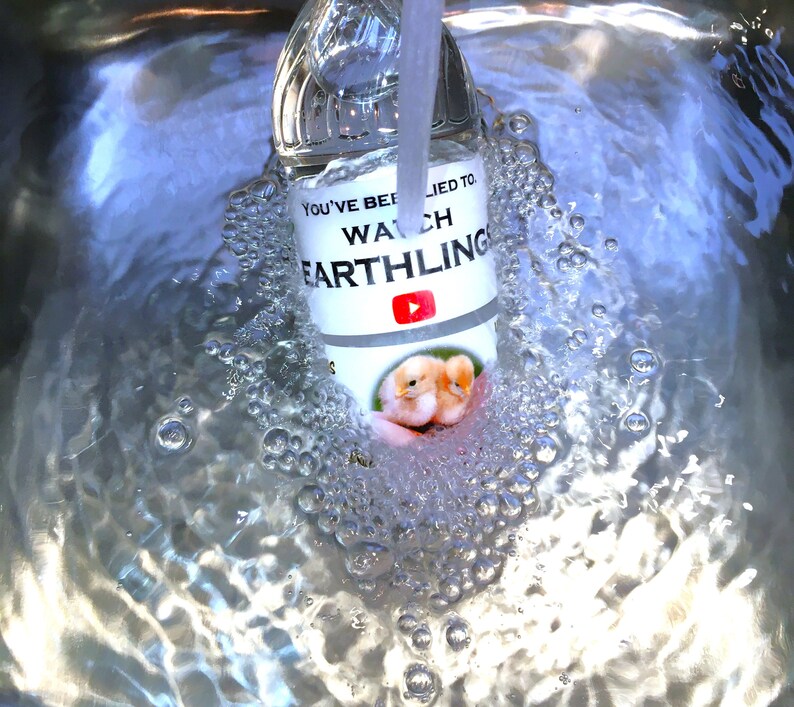May include: A clear glass bottle with a white label that says "You've been lied to. Watch Earthling" with a YouTube logo. The bottle is submerged in water with bubbles forming around it.