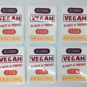 Op de afbeelding: Zes witte vierkante stickers met de tekst "Vegan worden is geen trend, het is een ontwaken" in rood, oranje en paars.