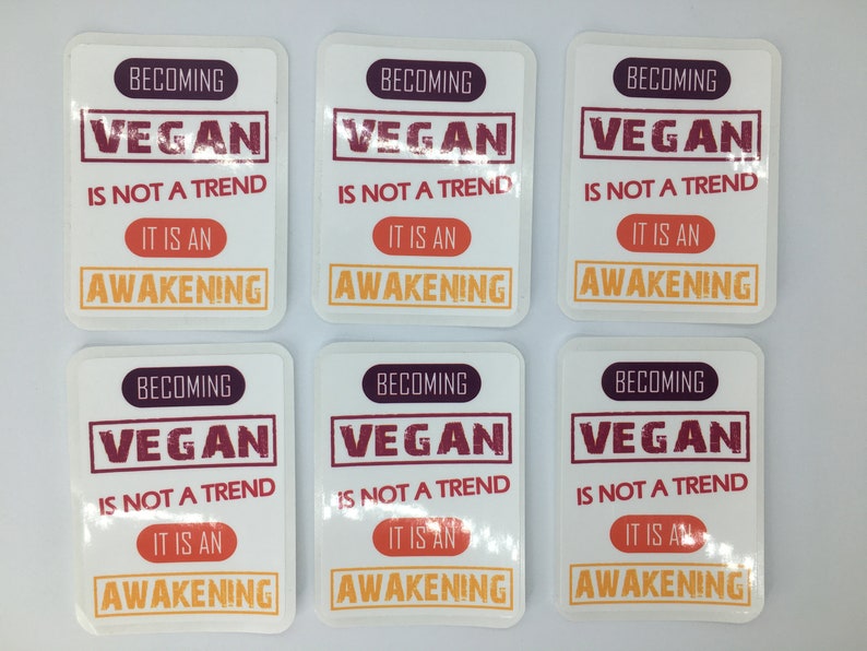 Op de afbeelding: Zes witte vierkante stickers met de tekst "Vegan worden is geen trend, het is een ontwaken" in rood, oranje en paars.