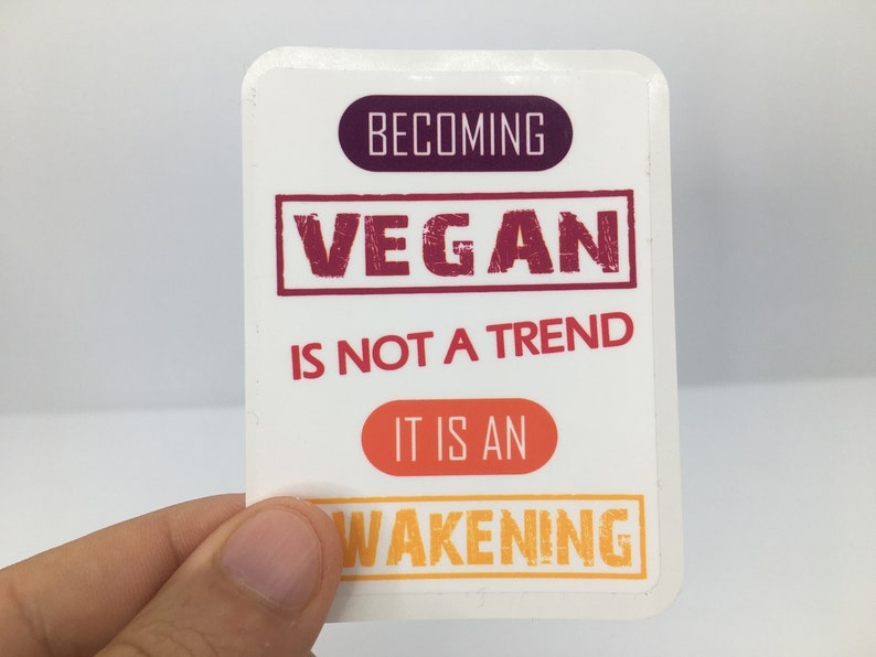 Op de afbeelding: Witte sticker met de tekst "Vegan worden is geen trend, het is een ontwaken" in rode, oranje en gele letters.