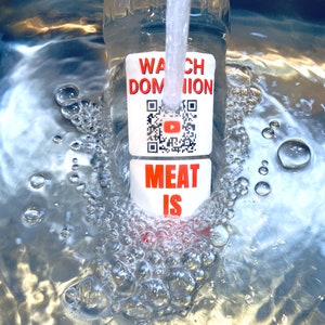 Pode incluir: Uma garrafa de pl&aacute;stico transparente com um r&oacute;tulo branco que diz "Watch Dominion Meat Is" e um c&oacute;digo QR com um bot&atilde;o de reprodu&ccedil;&atilde;o do YouTube vermelho. A garrafa est&aacute; sendo enchida com &aacute;gua e bolhas est&atilde;o se formando.