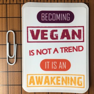 Op de afbeelding: Witte sticker met de tekst "Vegan worden is geen trend, het is een ontwaken" in een kleurenschema van rood, oranje en geel.