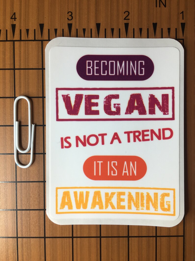 Op de afbeelding: Witte sticker met de tekst "Vegan worden is geen trend, het is een ontwaken" in een kleurenschema van rood, oranje en geel.