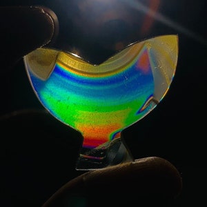 May include: A rainbow iridescent glass object shaped like a bird with a long, thin beak. The object is made of clear glass with a rainbow iridescent coating.