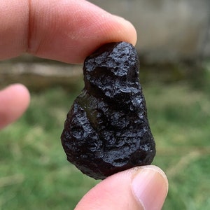 Puede incluir: Una roca de forma irregular, de color negro y ligeramente verde, con una superficie rugosa y texturizada.