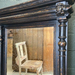 May include: A black antique mirror with a carved wooden frame and a distressed finish. The mirror reflects a wooden chair.