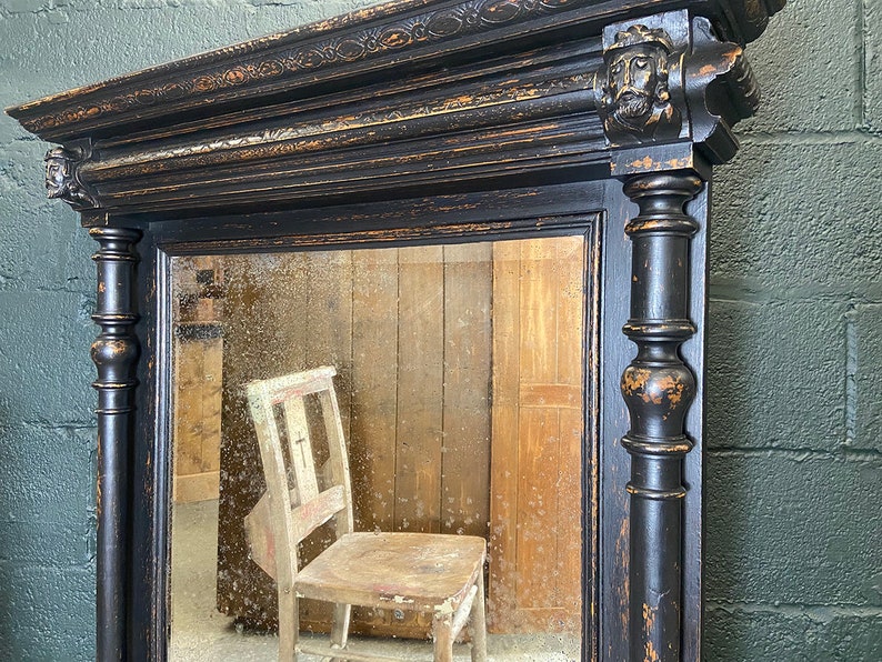 May include: A black antique mirror with a carved wooden frame and a distressed finish. The mirror reflects a wooden chair.