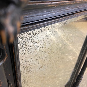 May include: A black wooden mirror with a distressed finish and a beveled glass mirror. The mirror has a decorative frame with a carved design.