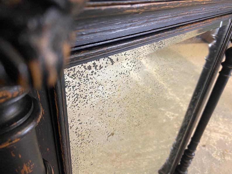 May include: A black wooden mirror with a distressed finish and a beveled glass mirror. The mirror has a decorative frame with a carved design.