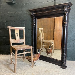 May include: A black antique mirror with a decorative frame and a distressed finish. The mirror is reflecting a wooden chair and a pheasant.