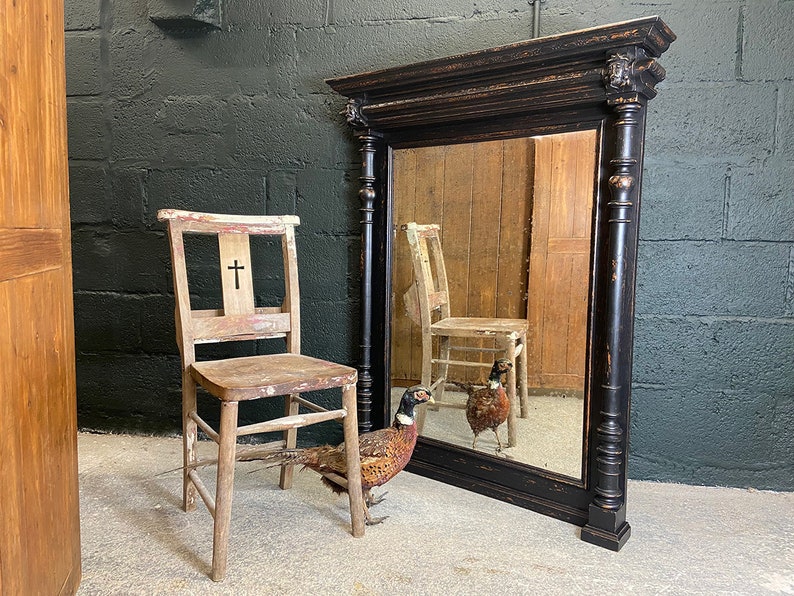 May include: A black antique mirror with a decorative frame and a distressed finish. The mirror is reflecting a wooden chair and a pheasant.