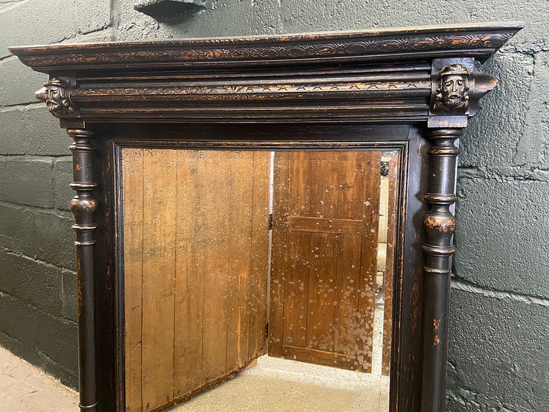 May include: A black wooden mirror with ornate carvings and a distressed finish. The mirror has a rectangular frame with a beveled edge and a simple, clear glass reflection.