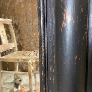 May include: A black wooden framed mirror with a distressed finish. The mirror has a slightly cloudy appearance and reflects a wooden chair.