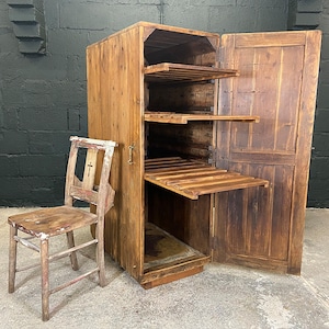 May include: A wooden cabinet with a door that opens to reveal shelves. The cabinet is made of reclaimed wood and has a rustic look. There is a wooden chair in front of the cabinet.