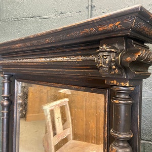 May include: A black antique mirror with a carved wooden frame and ornate details. The mirror has a distressed finish and a rectangular shape.