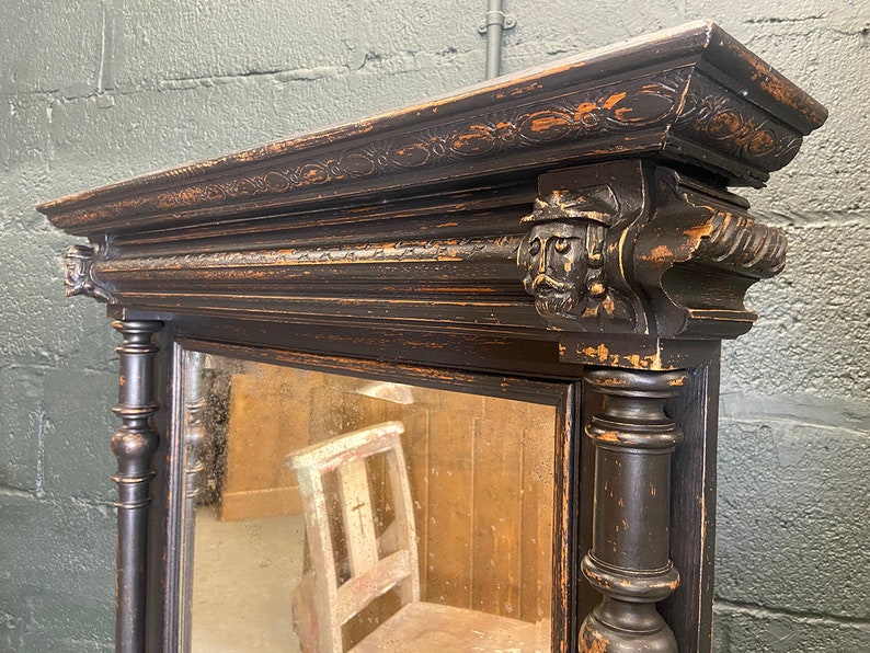 May include: A black antique mirror with a carved wooden frame and ornate details. The mirror has a distressed finish and a rectangular shape.