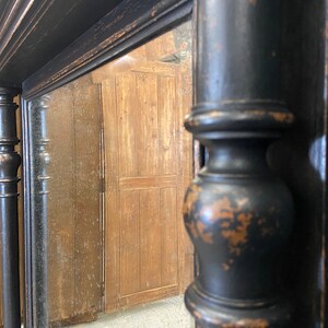 May include: A black antique mirror with a decorative frame. The frame has a distressed finish and features ornate details. The mirror is reflecting a wooden surface.