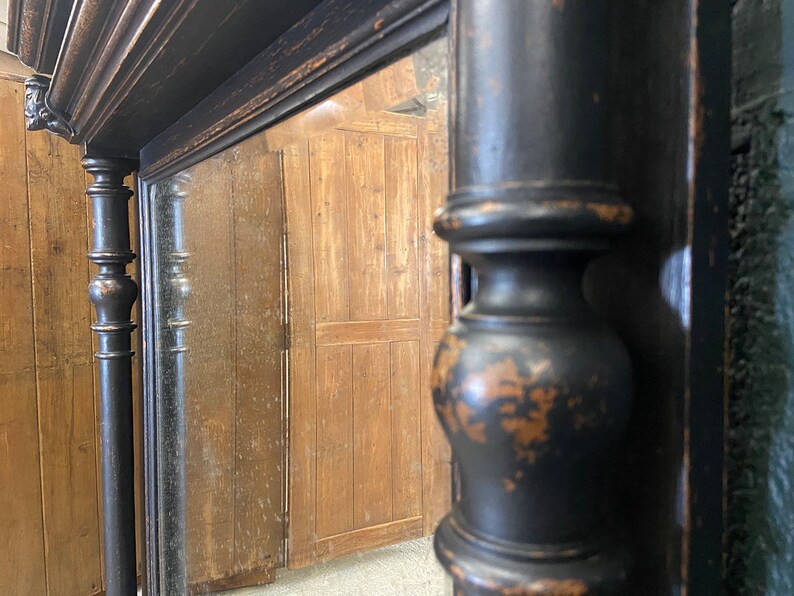 May include: A black antique mirror with a decorative frame. The frame has a distressed finish and features ornate details. The mirror is reflecting a wooden surface.
