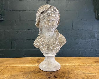 May include: A gray stone bust sculpture of a person with a draped cloth over their shoulders. The bust is on a pedestal.