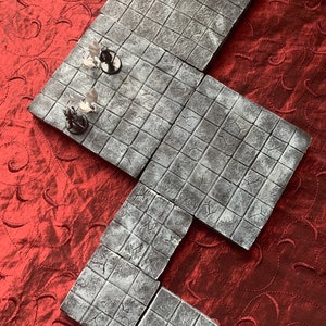 Puede incluir: Un conjunto de cinco baldosas cuadradas grises y blancas con un patrón de cuadrícula. Las baldosas están hechas de un material texturizado y están diseñadas para ser utilizadas como un tablero de juego.