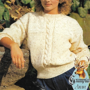 May include: A white cable knit sweater with a speckled pattern. The sweater has a cable knit design on the front and a crew neck.