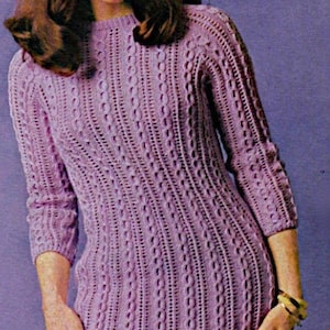 May include: A purple knitted dress with a cable knit pattern. The dress has long sleeves and a round neckline.