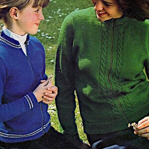 Pode incluir: Duas pessoas vestindo jaquetas de zíper de tricô. A pessoa à esquerda está vestindo uma jaqueta azul com detalhes brancos. A pessoa à direita está vestindo uma jaqueta verde com um padrão de tricô trançado.