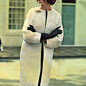 May include: A white crocheted coat with a black zip down the front. The coat has a textured, woven design and is being worn by a person with short, dark hair.