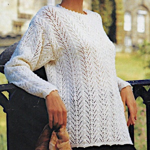 May include: A white knitted jumper with a delicate lace pattern. The jumper has a round neckline and long sleeves.