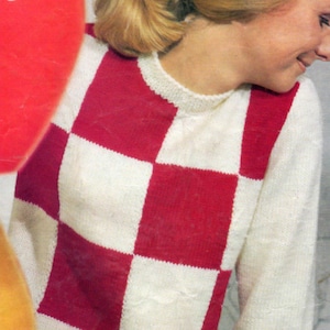Könnte beinhalten: Ein gestrickter Pullover mit einem rot-weißen Schachbrettmuster auf der Vorderseite. Der langärmlige Pullover hat einen Rundhalsausschnitt und ist aus einem weichen, strukturierten Garn gefertigt. Der untere Teil des Bildes zeigt einen roten Rock.