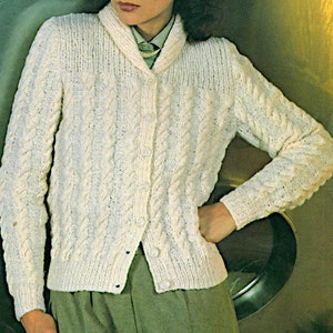 May include: Cream-colored cable-knit cardigan with a shawl collar and button closure. The long-sleeved sweater features a textured pattern and is worn over a green collared shirt and green pants. The cardigan is a classic style.