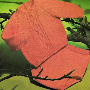 May include: A knitted baby sweater and pants set in a light pink color. The sweater has a cable knit pattern and a round neckline. The pants are plain knit.