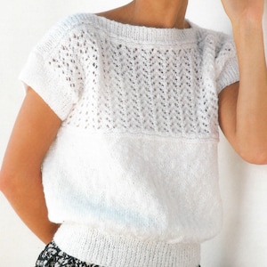 May include: A white knitted top with short sleeves and a delicate lace pattern around the neckline. The top has a relaxed fit and a slightly cropped length.