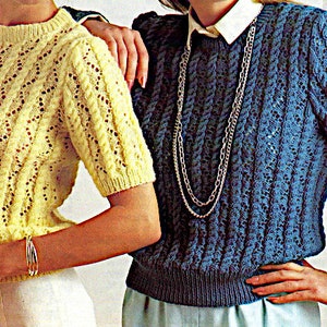 Könnte beinhalten: Zwei Frauen tragen Strickpullover. Die Frau links trägt einen gelben Pullover mit Zopfmuster. Die Frau rechts trägt einen blauen Pullover mit Zopfmuster und eine silberne Kettenkette.