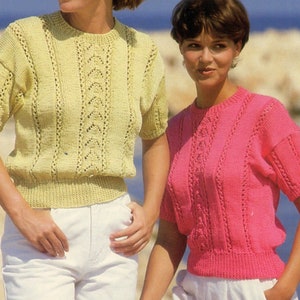 Puede incluir: Dos mujeres con tops de punto de manga corta con un diseño de punto de cable. El top de la izquierda es amarillo y el top de la derecha es rosa.