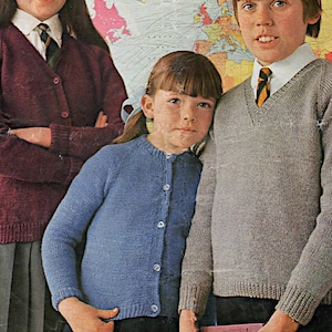 Puede incluir: Tres niños con cárdigans de punto. La niña de la izquierda lleva un cárdigan burdeos con una camisa blanca de cuello y una corbata a rayas. La niña del centro lleva un cárdigan azul claro con una camisa blanca abotonada. El niño de la derecha lleva un cárdigan gris con una camisa blanca de cuello y una corbata a rayas.