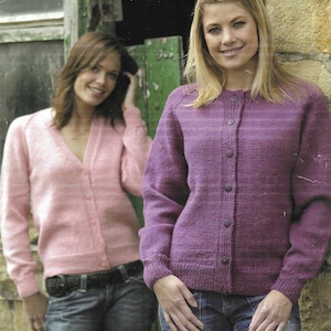 May include: Two women wearing cardigans. The woman on the left is wearing a pink cardigan and the woman on the right is wearing a purple cardigan. Both women are wearing jeans.