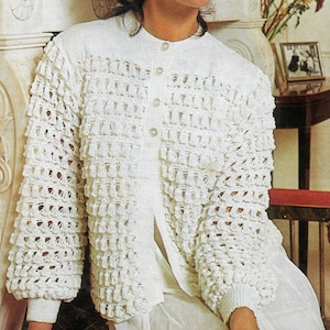 May include: White crocheted cardigan with a button-up front and long sleeves. The cardigan has a delicate, lacy pattern and a slightly flared silhouette.