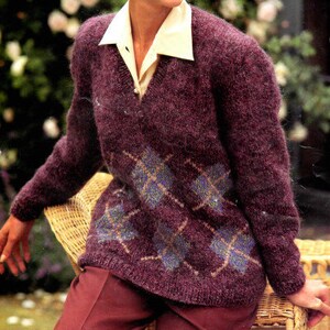 May include: A purple sweater with a diamond pattern in a lighter shade of purple. The sweater has a V-neck and is made of a soft, fuzzy material.