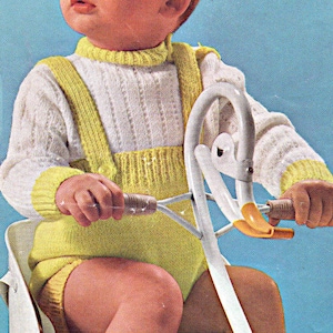 May include: A child wearing a white and yellow knitted sweater and overalls is riding a white toy bike with yellow handlebars.