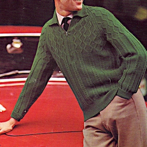 May include: A man wearing a green cable knit sweater with a zip and a dark tie. He is standing in front of a red car.