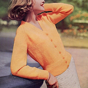 May include: A bright orange knitted cardigan with a v-neck and button closure. The cardigan is being worn by a person with short blonde hair.