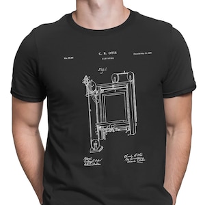 May include: Black t-shirt with a white print of a patent drawing for an elevator. The drawing shows a mechanical system with pulleys and ropes. The text on the print reads "C.R. OTIS ELEVATOR" and "Patented May 21, 1867".