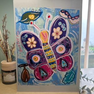 May include: A vibrant butterfly artwork on a grey card. The butterfly features purple, pink, and yellow wings with floral and heart patterns. The background is blue with white highlights. The words "Butterfly" and "Chrysalis" are visible.