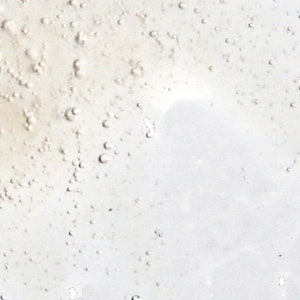 May include: Close-up of a clear, viscous liquid with numerous small bubbles. The liquid has a slightly yellowish tint and a smooth, reflective surface. The bubbles vary in size and are scattered throughout the liquid.