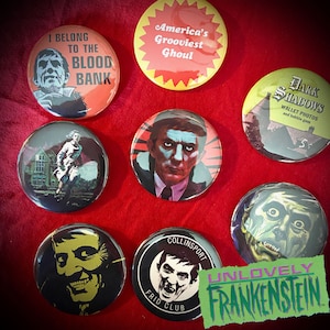 May include: Eight round buttons with various horror movie themes. The buttons feature images of characters and scenes from classic horror films, including "I Belong to the Blood Bank", "America's Grooviest Ghoul", "Dark Shadows", "Unlovely Frankenstein", and "Collinsport Frid Club".